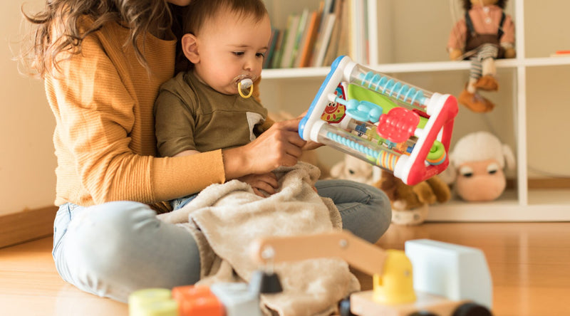 baby sitting in mum lap playing with toy|read our blog about toddler hitting and biting|dad reading bedtime story to son|mom and baby|sleep bundle deal